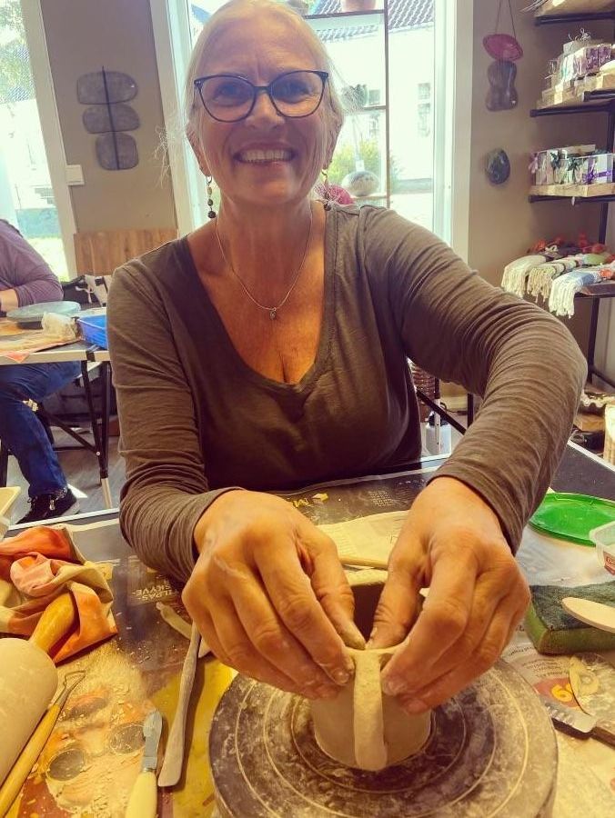 Kristina Hansen smiler mens hun former leire i et keramikkverksted.