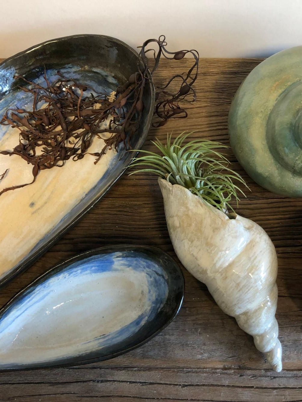 Keramikkfat og skjellformede gjenstander i naturfarger, dekorert med tang og plante.